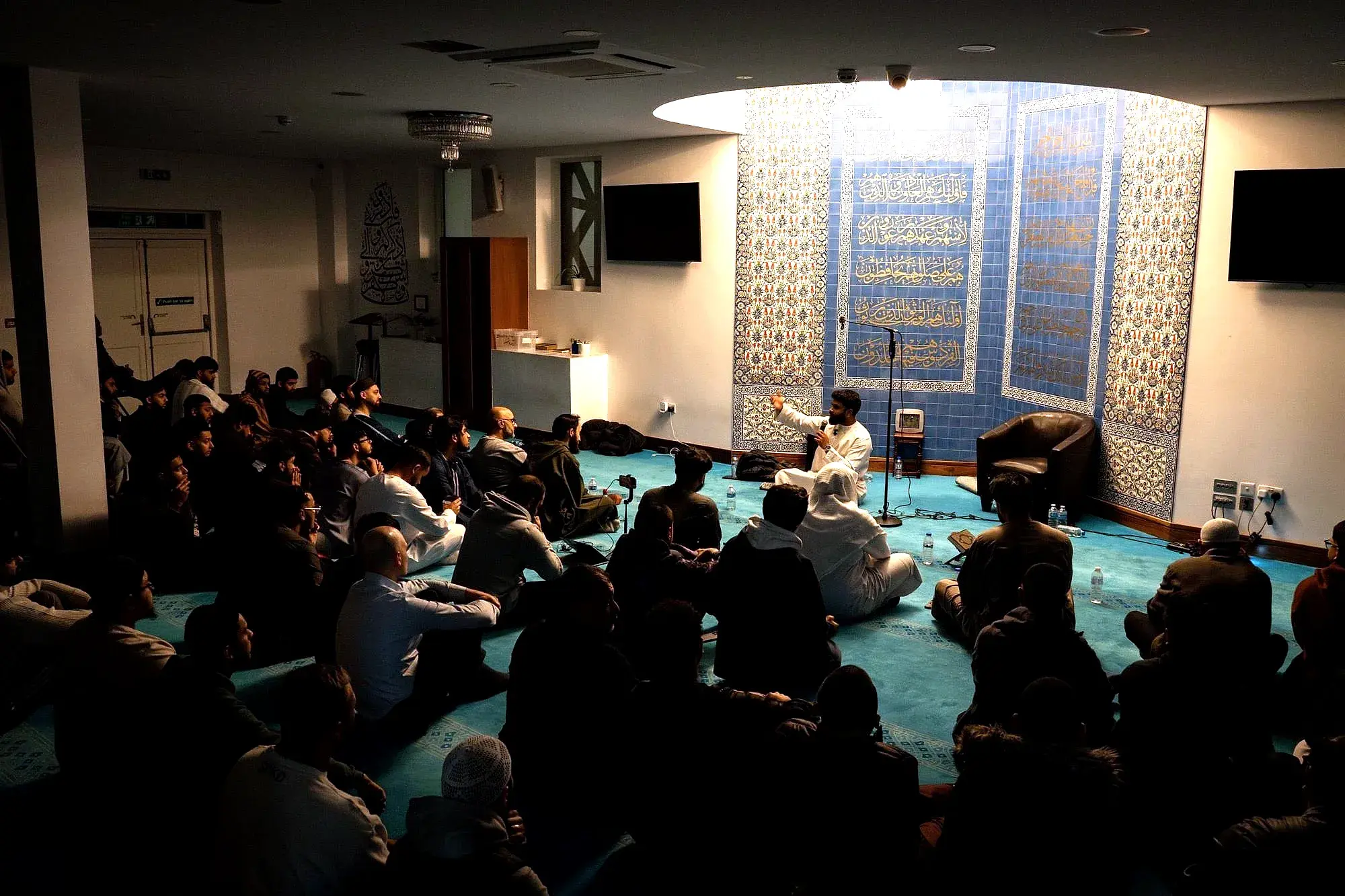 A scholar addressing a full room of ATTQ students in a masjid